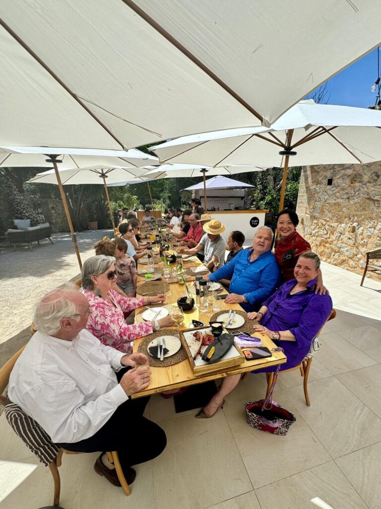 Lange gedeckte Tafel unter weißen Sonnenschirmen im Garten des Lume und Co in Palma, Gäste sitzen an der Tafel.