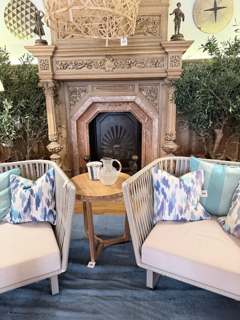 Alter verzierter Steinkamin im Rialto Living in Palma, davor zwei helle Sessel mit gemusterten Kissen und ein runder Holztisch.