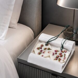 Carrière Frères Botanical Palets Damask Rose Schachtel auf einem Hotelnachttisch neben Bett, Lampe und Buch