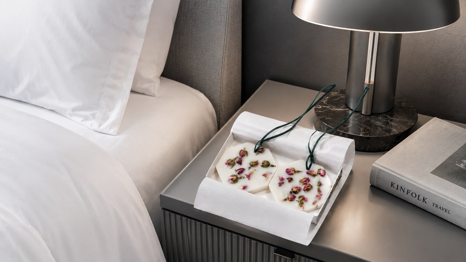 Carrière Frères Botanical Palets Damask Rose Schachtel auf einem Hotelnachttisch neben Bett, Lampe und Buch