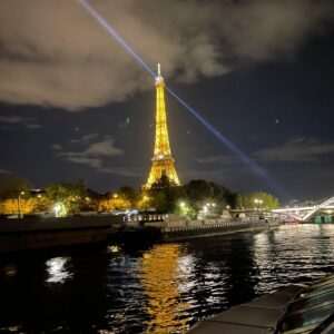 Der beleuchtete Eiffelturm mit Leuchtturm-Scheinwerfer bei Nacht ueber der Seine