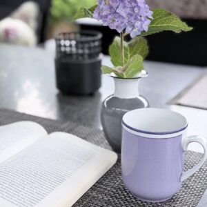 Reichenbach Becher in flieder auf der Terrasse, daneben eine Hortensie in einer grauen Reichenbach-Vase, links ein aufgeschlagenes Buch