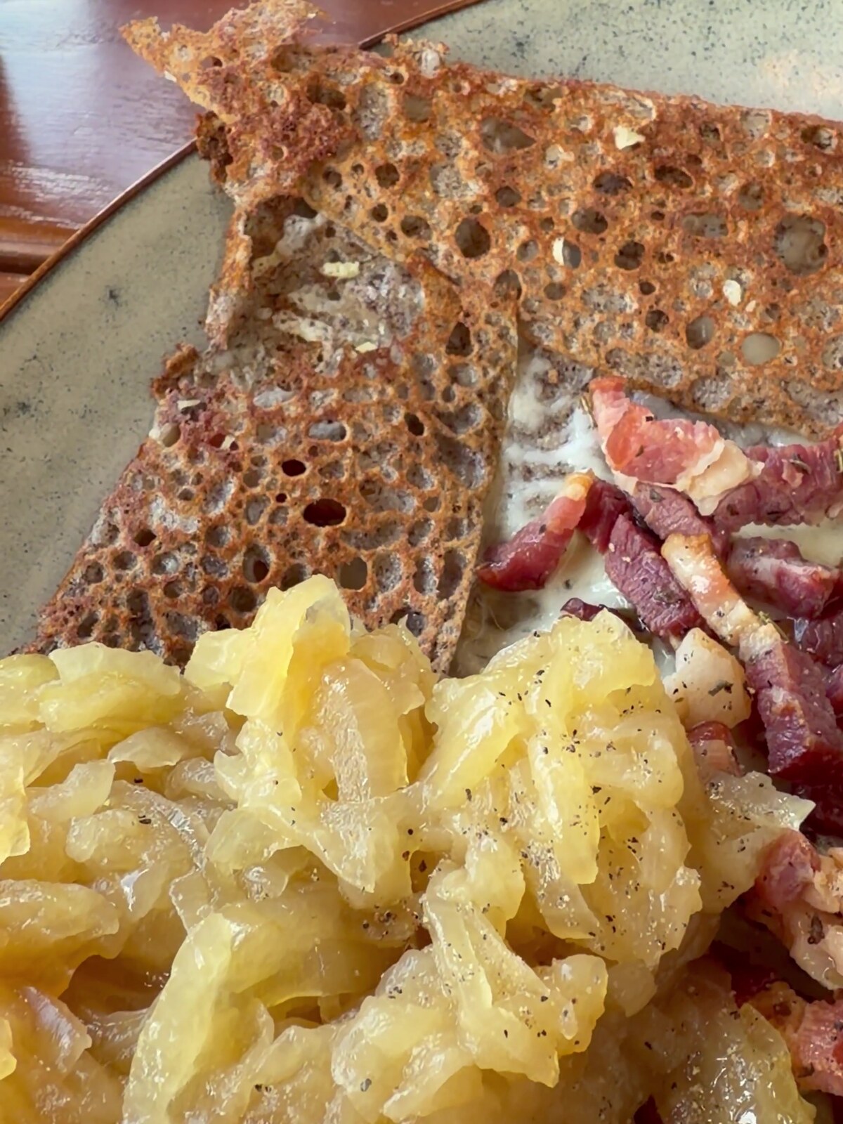 Nahaufnahme der Weißwein-Zwiebelkonfitüre und des gebratenen Specks auf der Galette