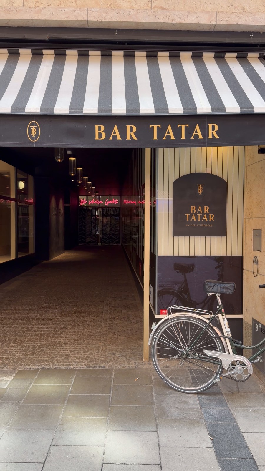 Eingang der Bar Tatar in München mit gestreifter Markise und langem Durchgang