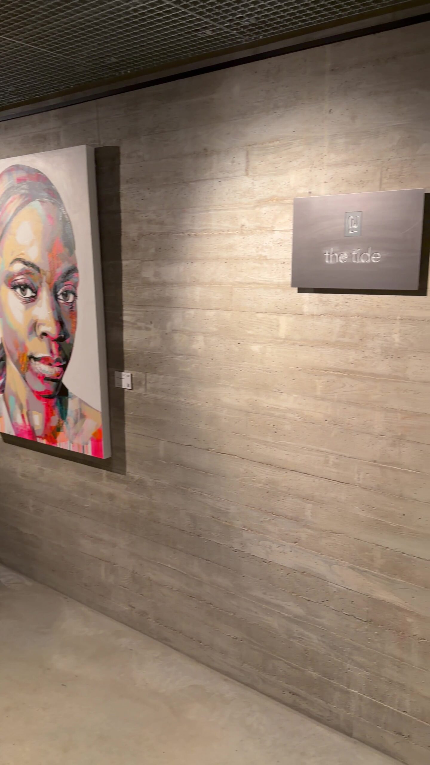 The Tide hotel signage on a raw concrete wall next to a colourful portrait painting in HafenCity Hamburg