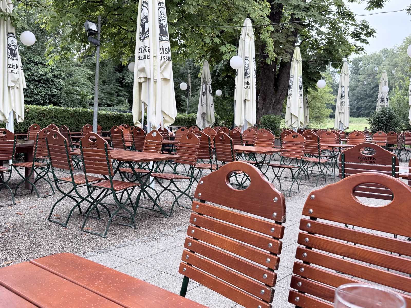 Leerer Biergarten der Emmeramsmühle in München mit roten Klappstühlen und Kastanien