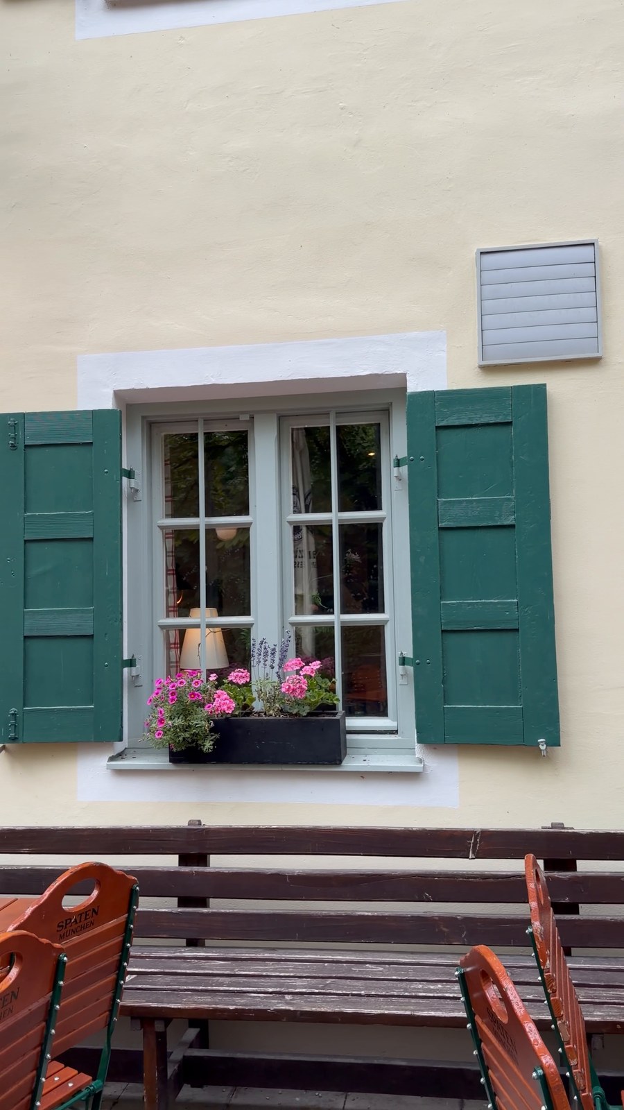 Außenansicht der Emmeramsmühle in München mit grünen Fensterläden und Blumenkasten