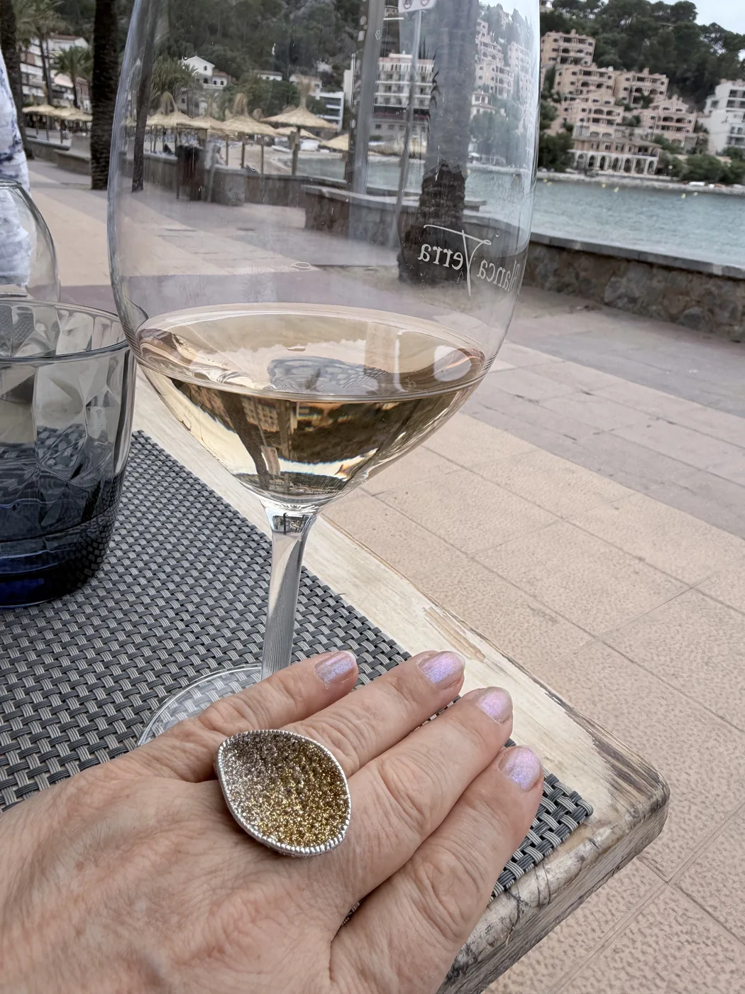 Hand wearing the KMO ALANA ring in yellow next to a glass of Can Axartell at the harbour of Port de Sóller.