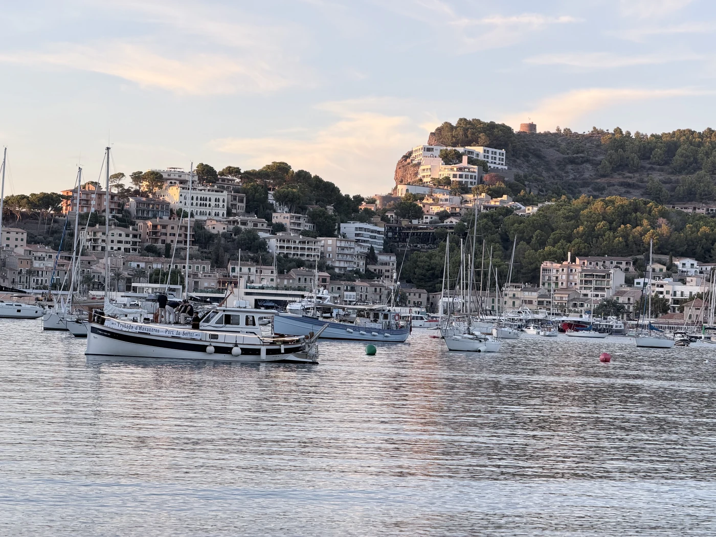 Boats in the harbour of Port de Sóller in front of the lit hillside.