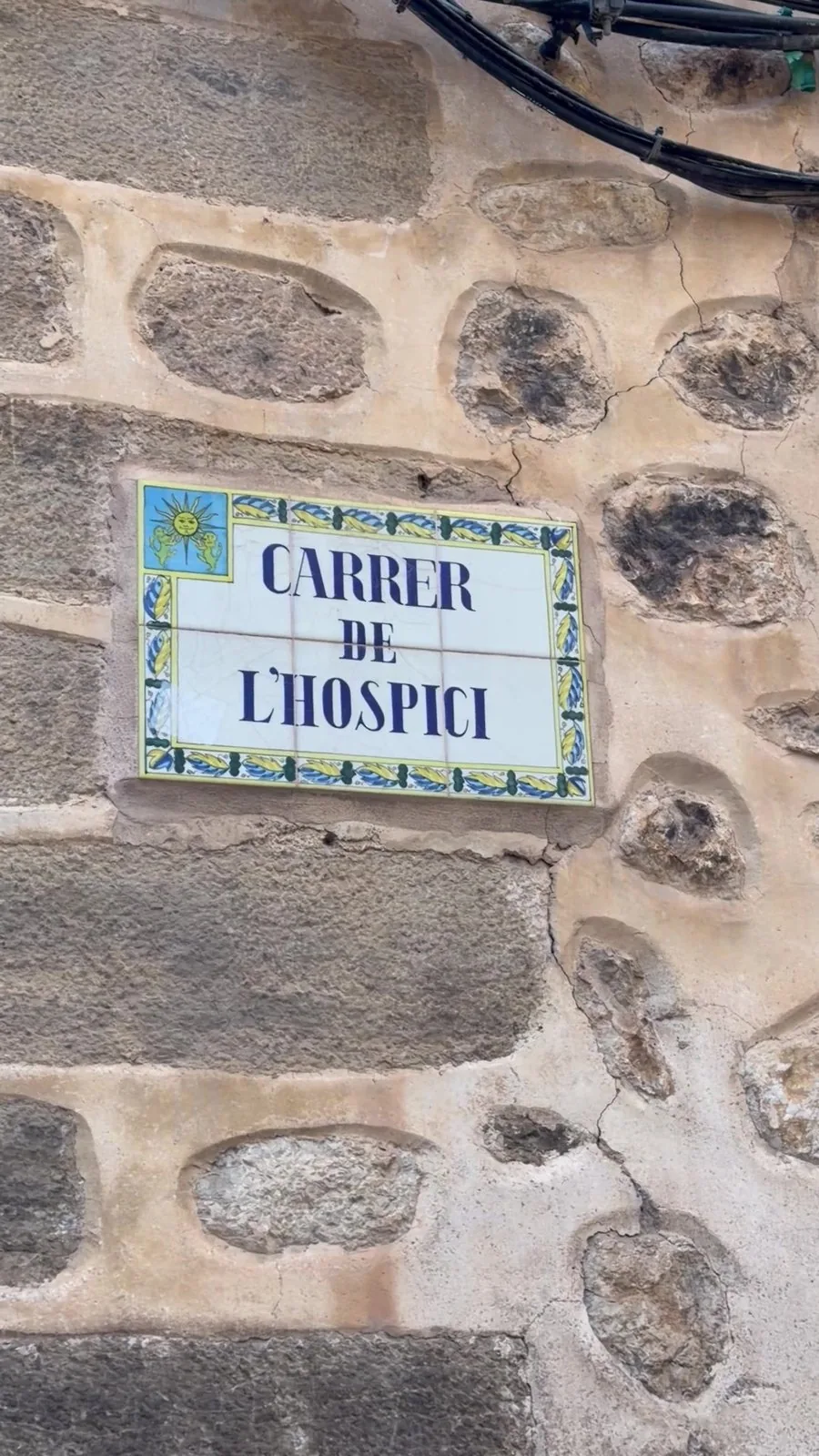 Keramikkachel mit der Aufschrift Carrer de l Hospici an einer Bruchsteinmauer in Sóller