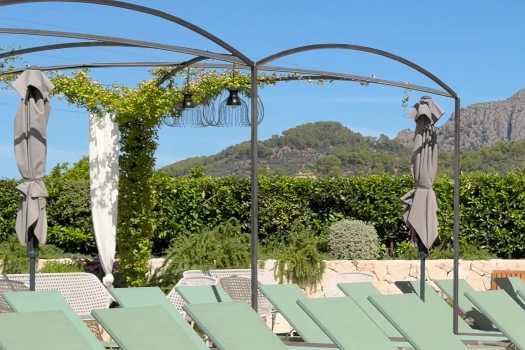 Terrasse mit Pergola und salbeigrünen Liegen im Hotel Alcázar in Sóller, dahinter die Berge.