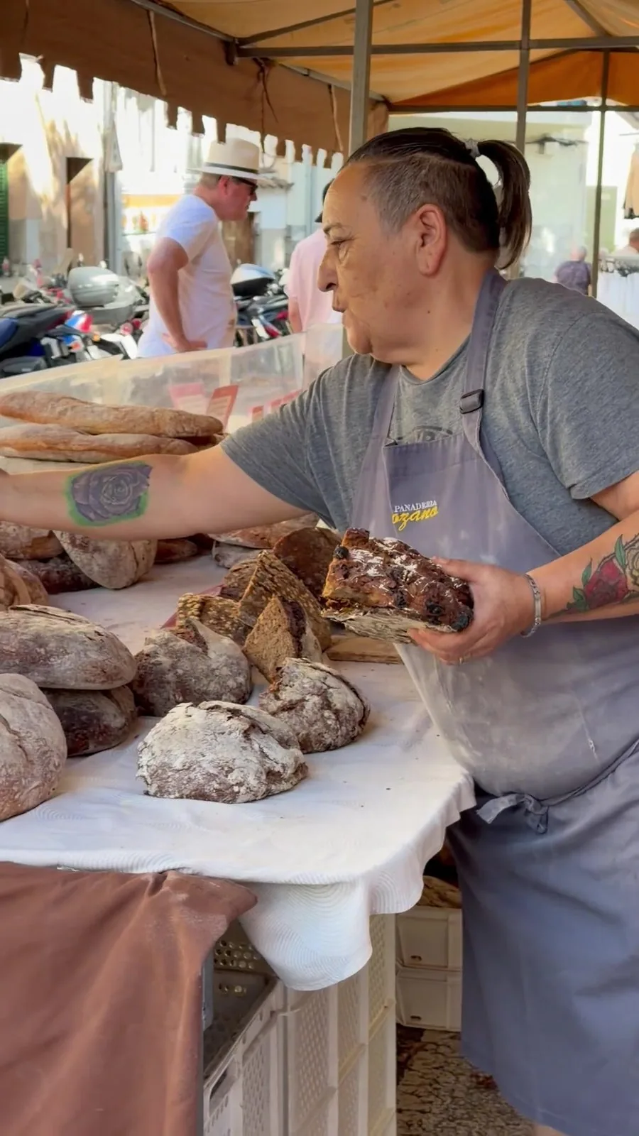 Verkäuferin am Brotstand auf dem Markt in Sóller legt große dunkle Brotlaibe auf ein weißes Tuch