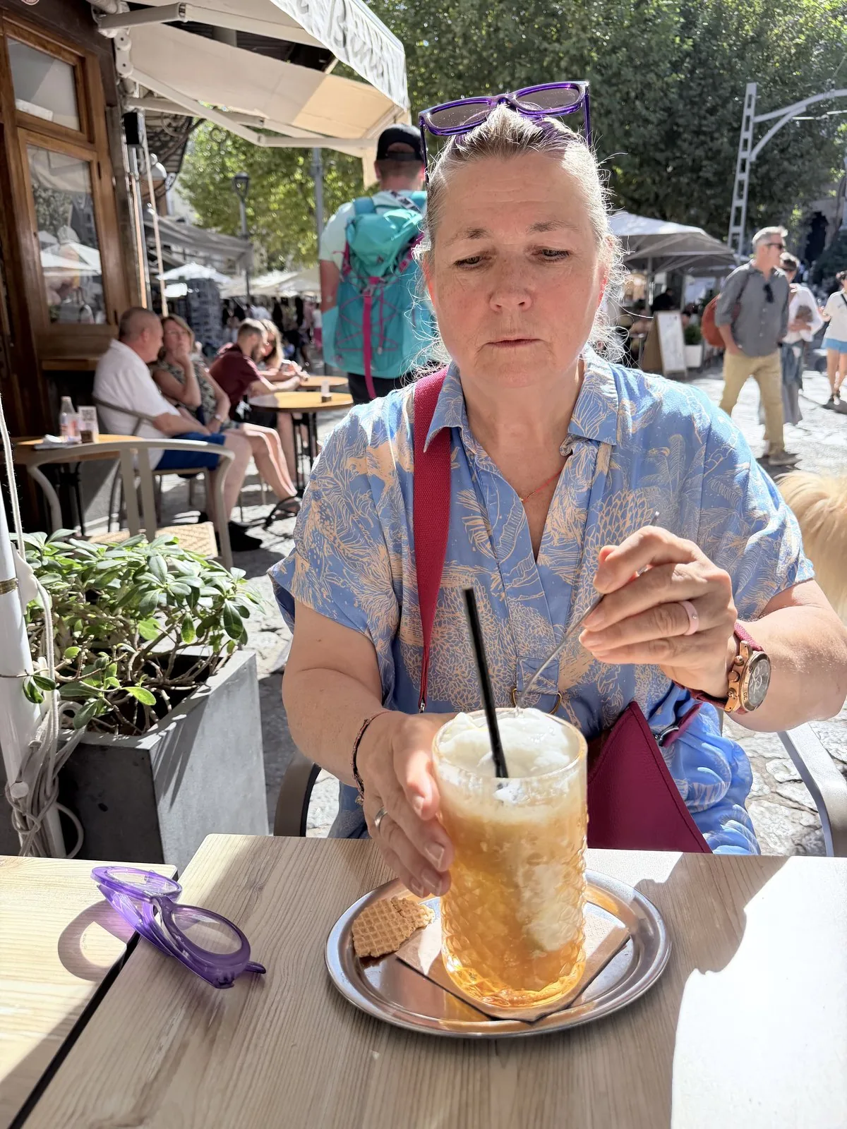 Sóller Orange Bomb im Glas auf dem Tisch der El Petit Cafeteria in Sóller, daneben eine violette Lesebrille von Doubleice, am Handgelenk eine Uhr von a cuckoo moment mit fuchsiafarbenem Rochenlederarmband