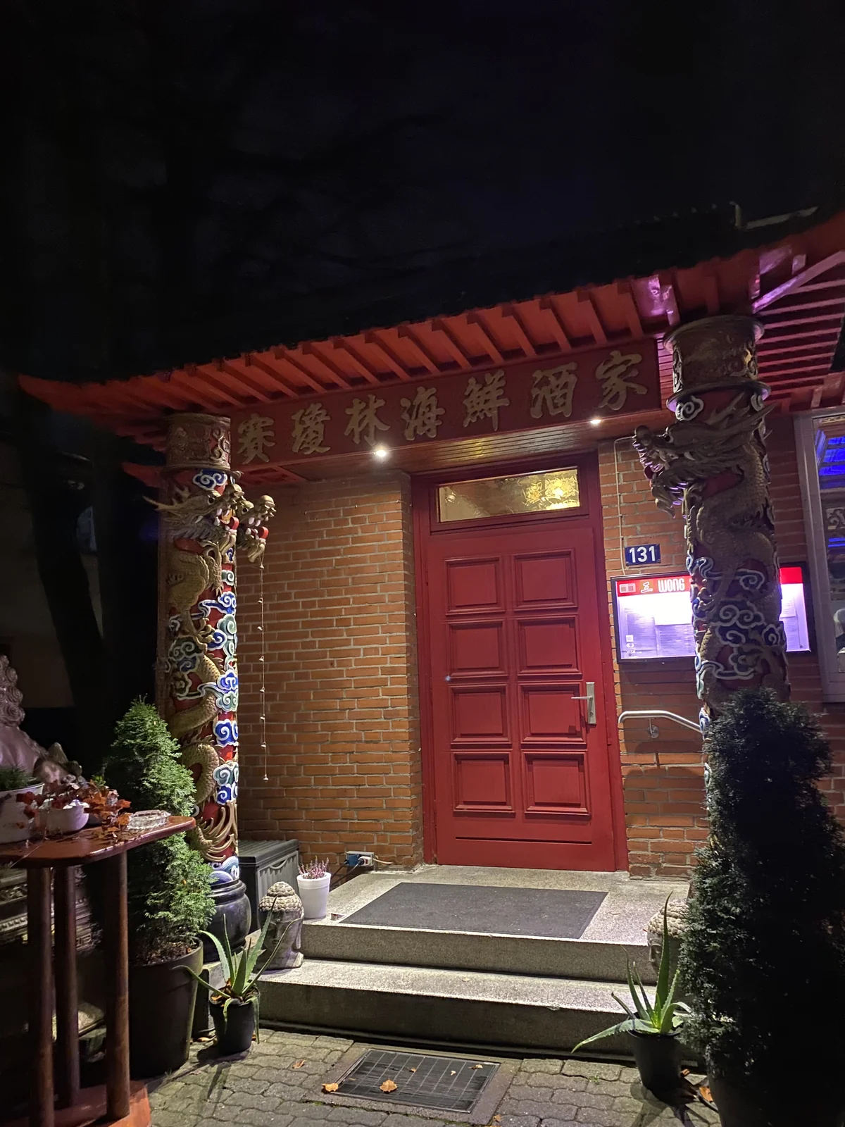 The lit entrance of Wong restaurant at Langenhorner Chaussee 131 in Hamburg, with its red door, dragon columns and golden lettering