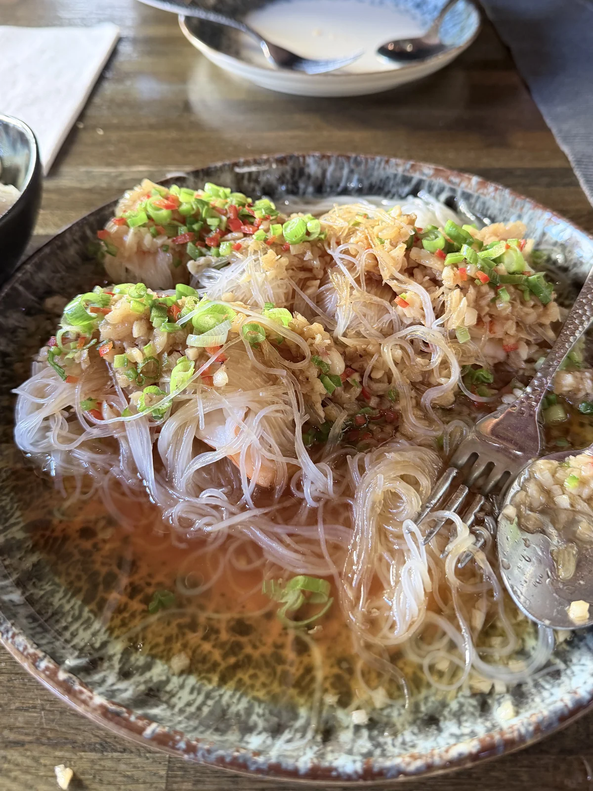 Glasnudeln mit Scampi, darauf von Hand geschnittene Frühlingszwiebeln, Chili und Knoblauch, in einer dunklen Schale im Restaurant Wong Hamburg
