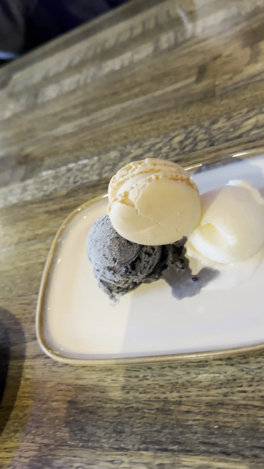 Black sesame ice cream and pale yuzu ice cream with a macaron on a plate at Wong restaurant in Hamburg