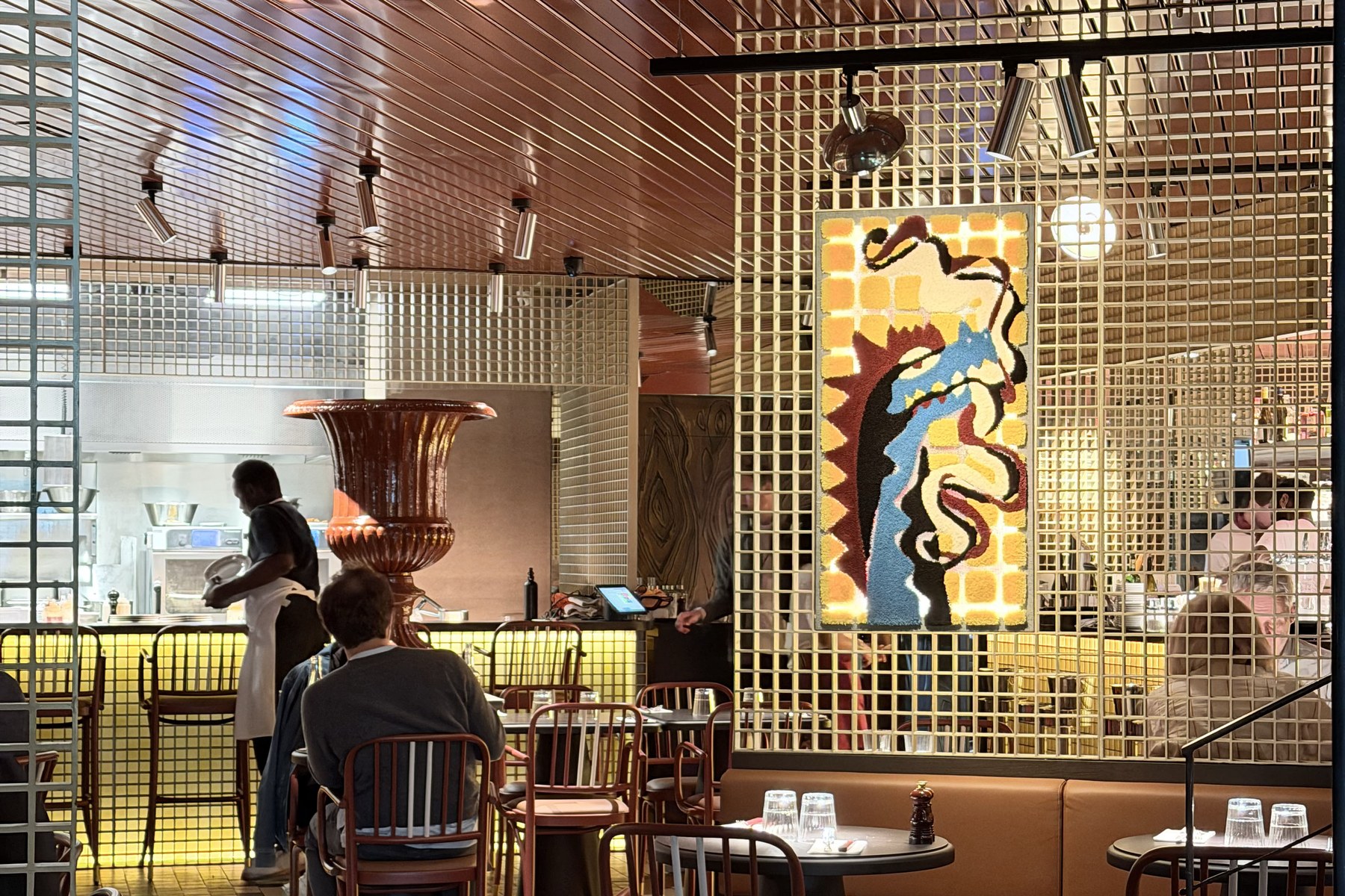 Dining room of the Fougue brasserie with a copper ceiling, a brass grille, the bar and a large colourful artwork