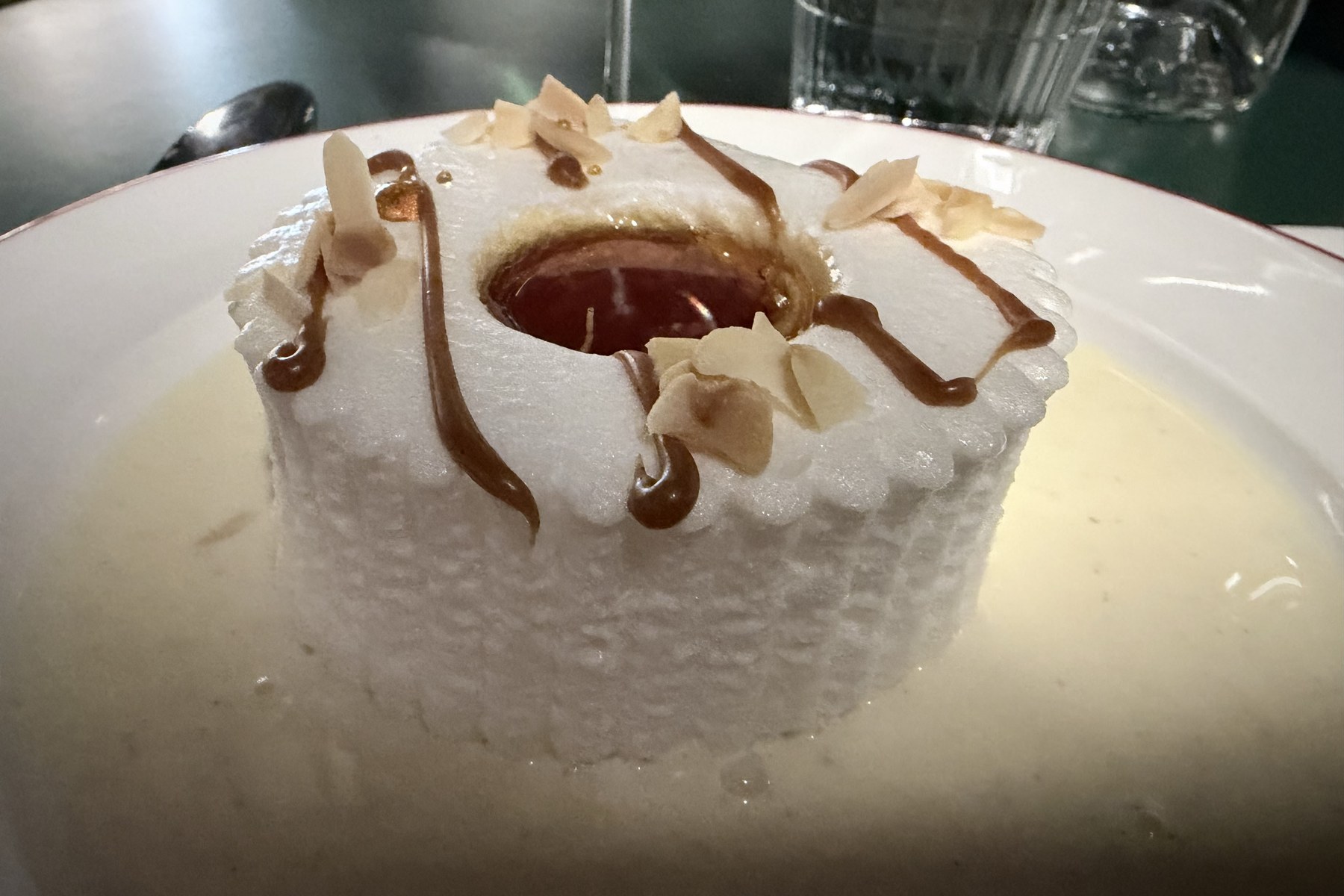 Île flottante als weißes Eischnee-Törtchen in Vanillesauce, in der Mitte eine Vertiefung mit Karamell, dazu Karamellfäden und Mandelblättchen