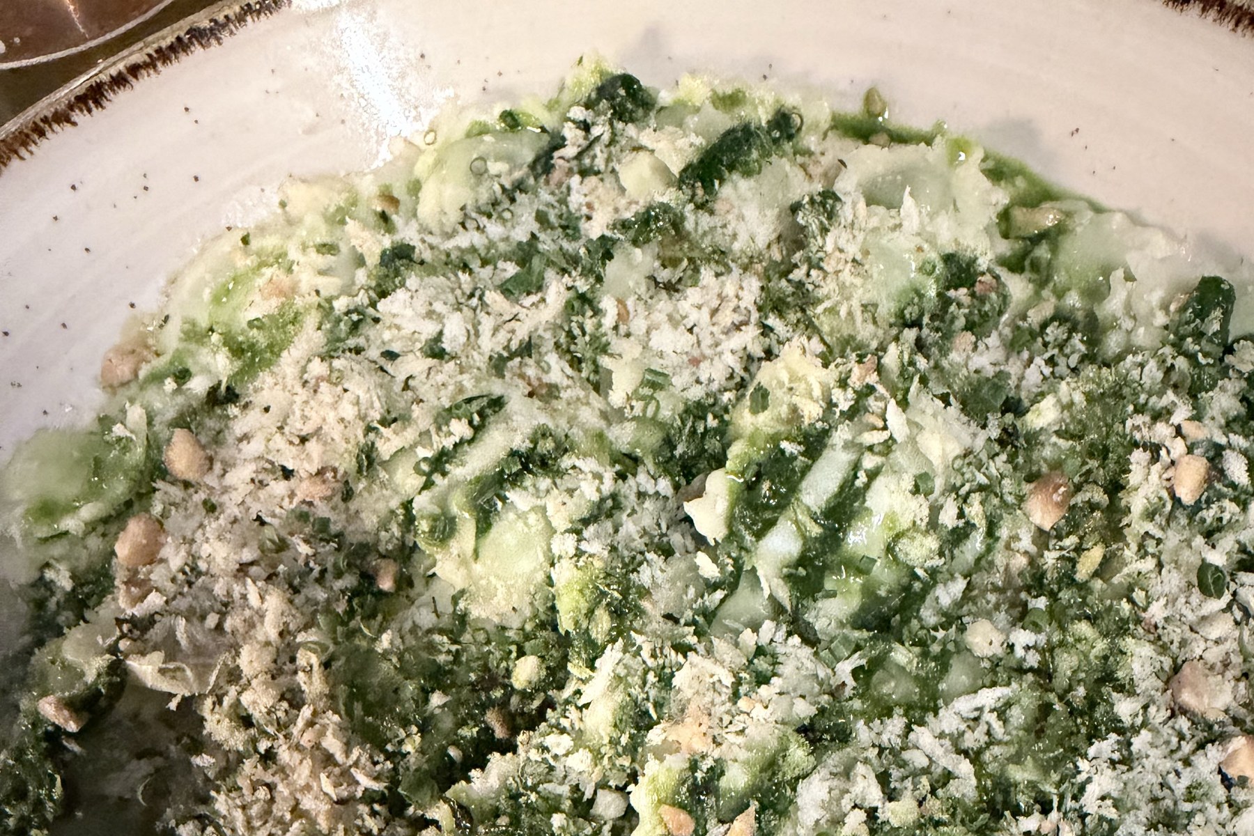 Ravioles du Dauphiné under a green sauce with pale crumbs in a deep plate