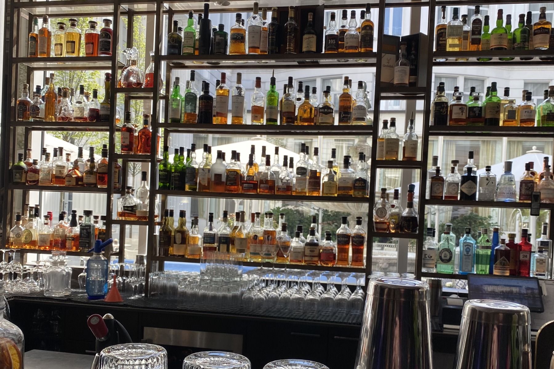 The counter of the Atlantic Bar with its tall bottle shelf, upturned glasses and a silver tray, photographed in 2024.