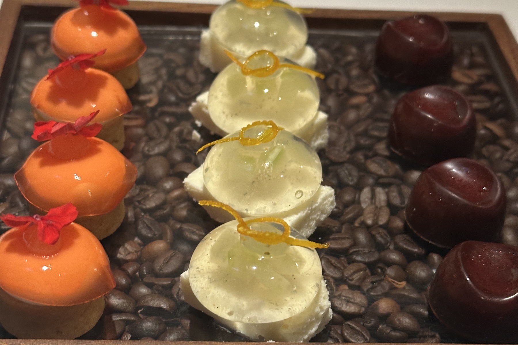Three kinds of petits fours set out in rows on a wooden tray filled with coffee beans.
