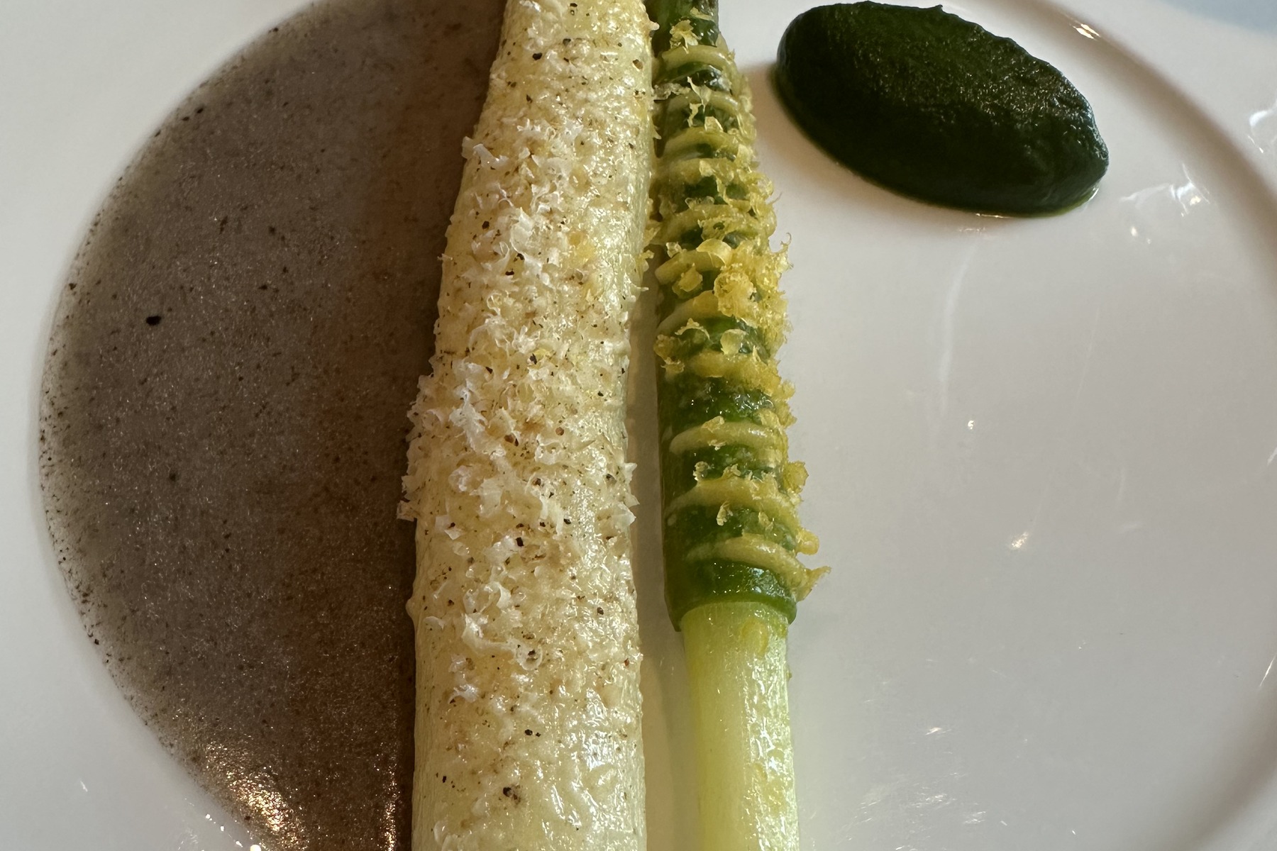 White asparagus with a crisp crust on a dark, foamy sauce, with a green dot of herbs beside it.