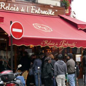 Rote Markise mit dem Schriftzug Le Relais de l'Entrecôte in der Rue Saint-Benoît in Paris, davor eine Warteschlange