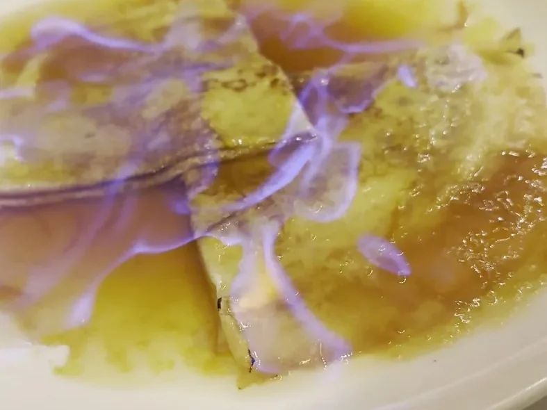 Brennende Crêpes Suzette mit blauer Flamme auf einem weißen Teller im Les Antiquaires in Paris