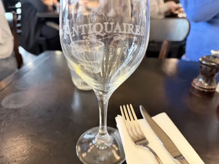 Weinglas mit eingraviertem Schriftzug LES ANTIQUAIRES auf einem dunklen Holztisch im Restaurant Les Antiquaires in Paris