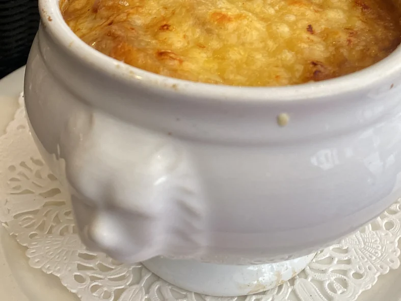 Zwiebelsuppe mit Käsekruste in einer weißen Terrine mit Löwenkopf im Les Antiquaires in Paris